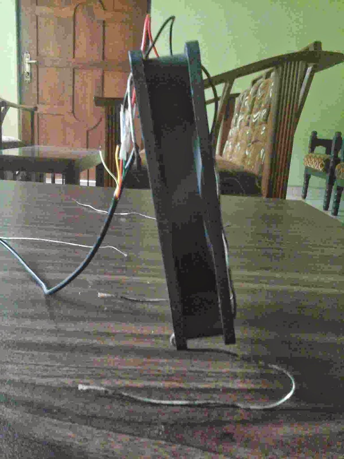 Dark rectangular object with multiple colored wires attached, standing upright on a wooden table